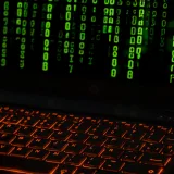 A laptop keyboard with orange backlight displaying green digital code symbols.