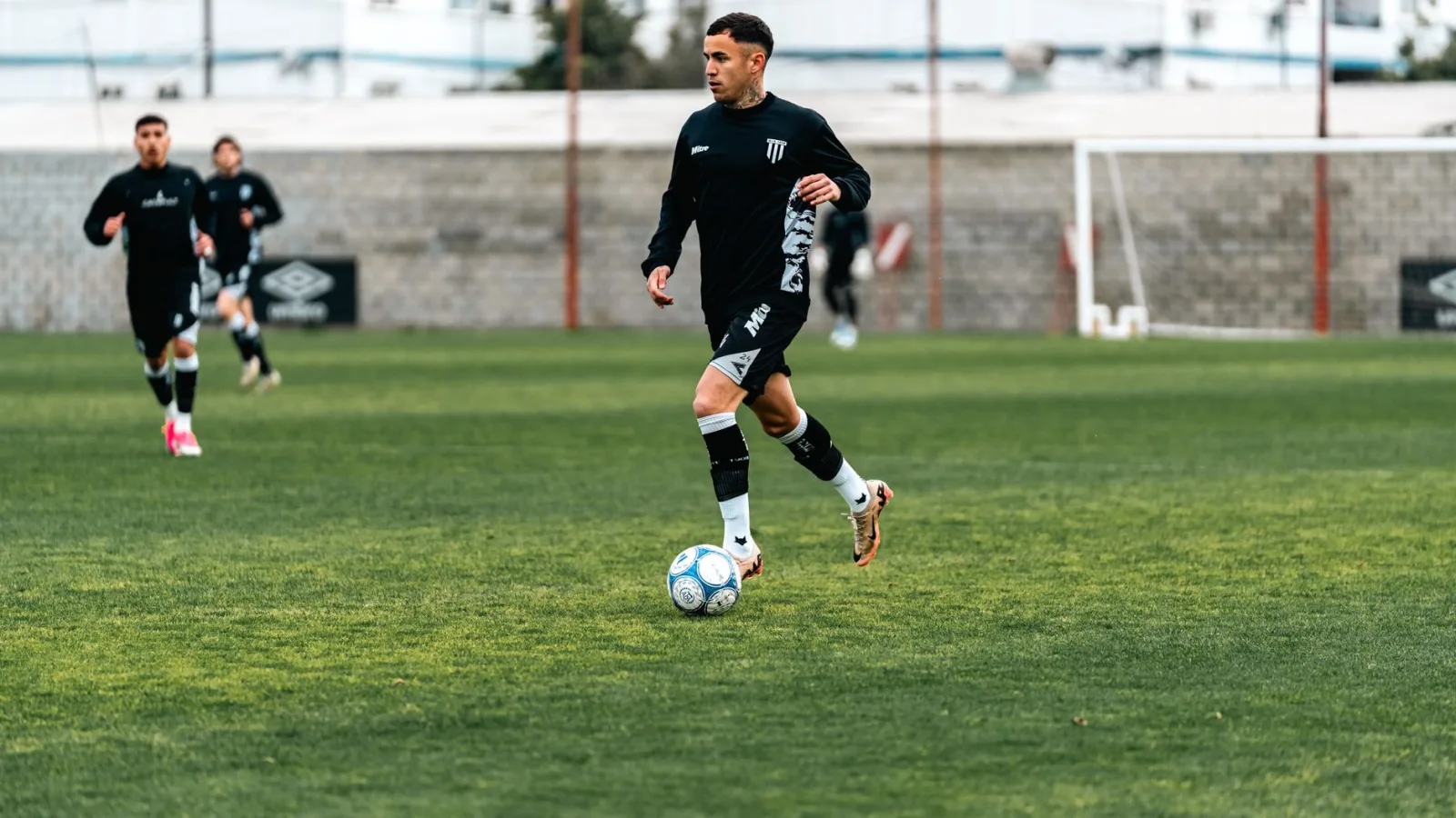 Atletas con uniformes negros practicando fútbol en un campo.