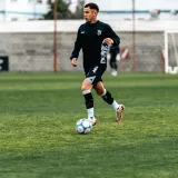 Atletas con uniformes negros practicando fútbol en un campo.