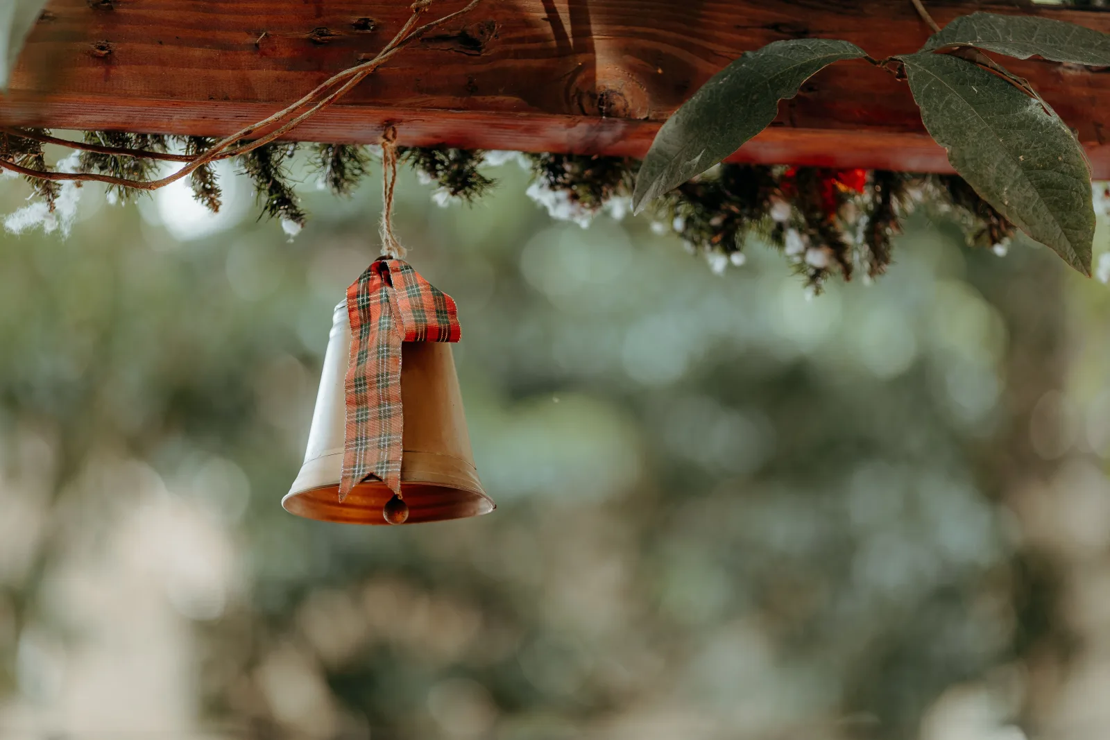 Una campana con un lazo de cuadros cuelga de una viga de madera, evocando un ambiente rústico y festivo.