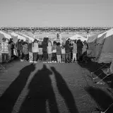 Black and white photo of a group gathered between tents in a Turkish refugee camp.