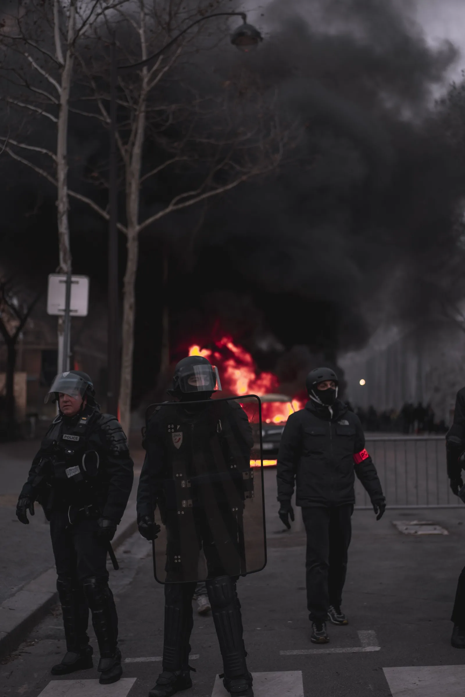 Policías antidisturbios equipados se enfrentan a un incendio en la calle durante una protesta urbana nocturna.