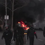 Policías antidisturbios equipados se enfrentan a un incendio en la calle durante una protesta urbana nocturna.