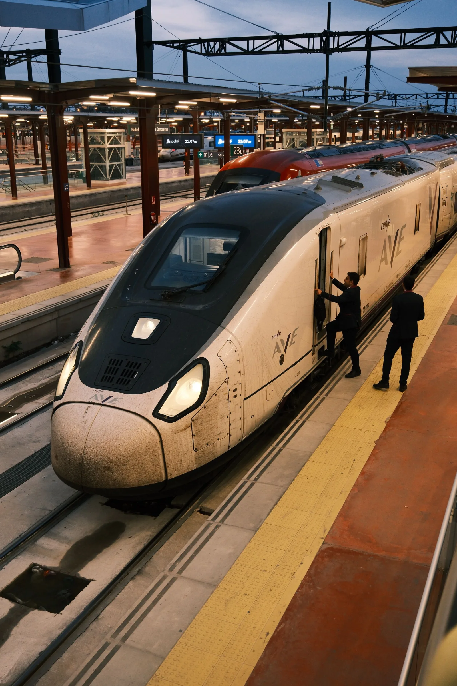 Un tren AVE de alta velocidad detenido en una plataforma urbana, con pasajeros subiendo a bordo.
