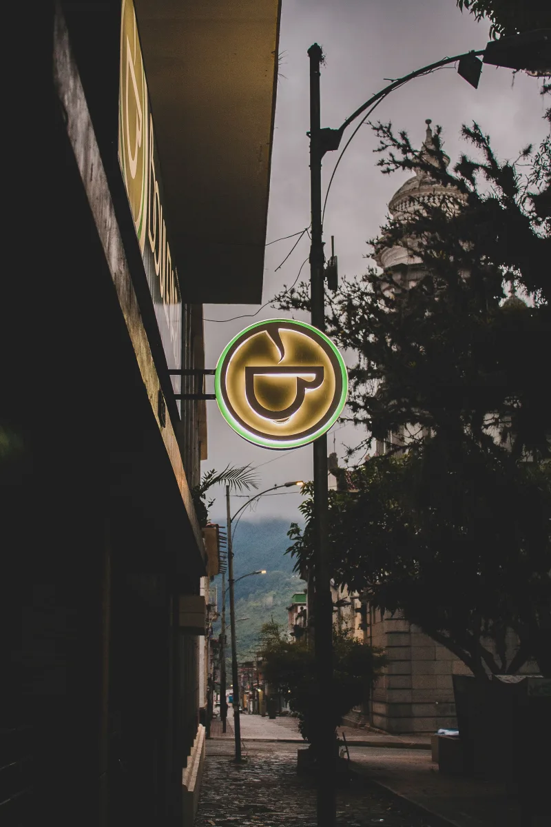 A glowing neon sign illuminates a quaint street in Mérida, Venezuela, at twilight.