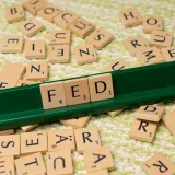 Fichas de Scrabble que forman la palabra «FED» en un atril verde, rodeadas de fichas dispersas sobre una superficie texturizada.
