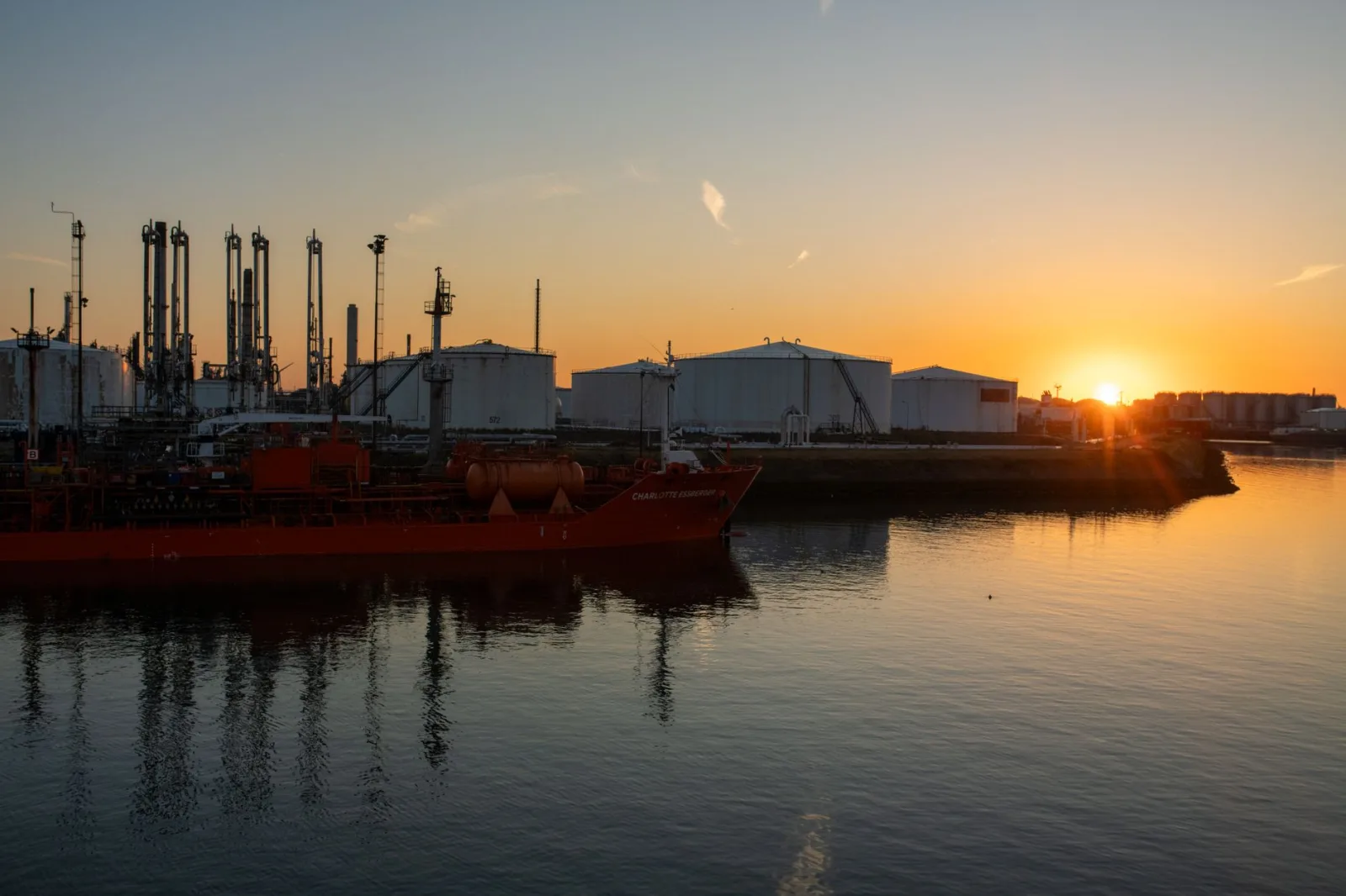 Una pintoresca vista de un puerto industrial y un buque cisterna al amanecer, que crean una silueta impresionante.
