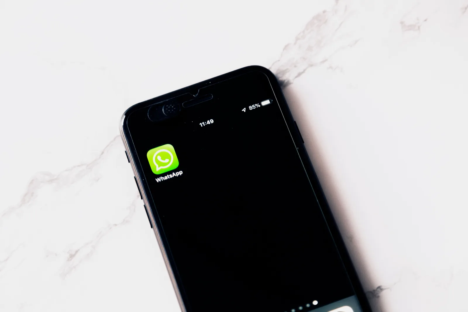 Imagen en primer plano de un teléfono inteligente que muestra WhatsApp sobre una mesa blanca.
