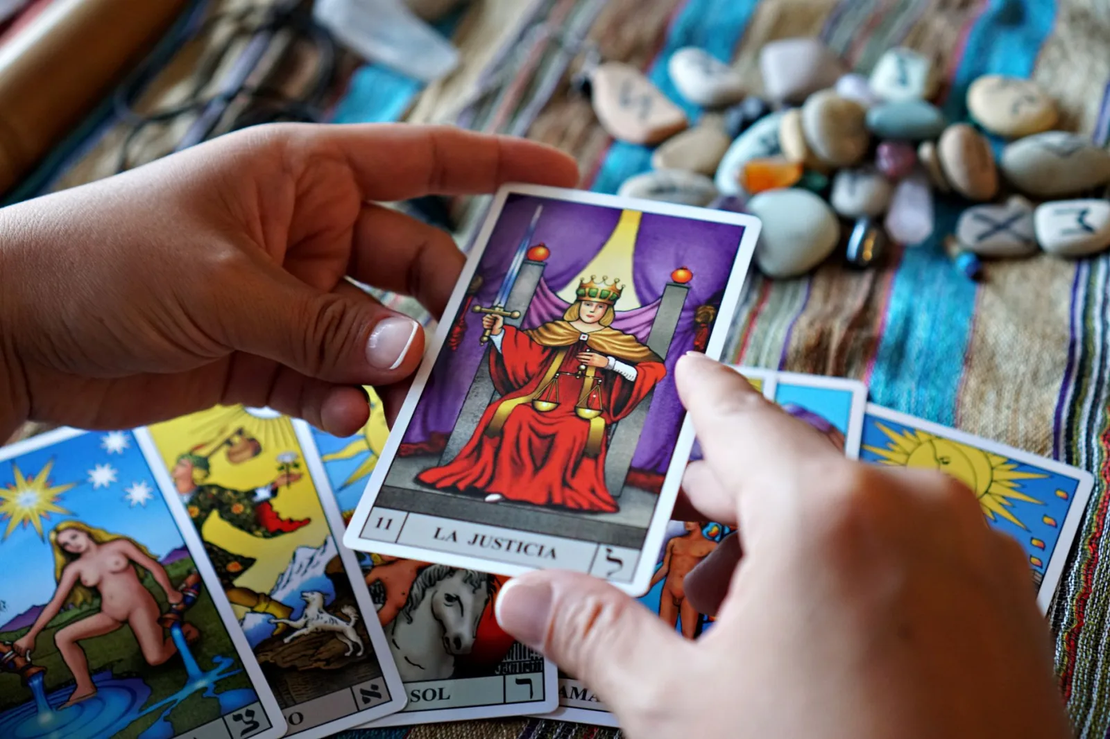 Manos sosteniendo una carta del tarot de la justicia sobre una tela colorida durante una lectura.