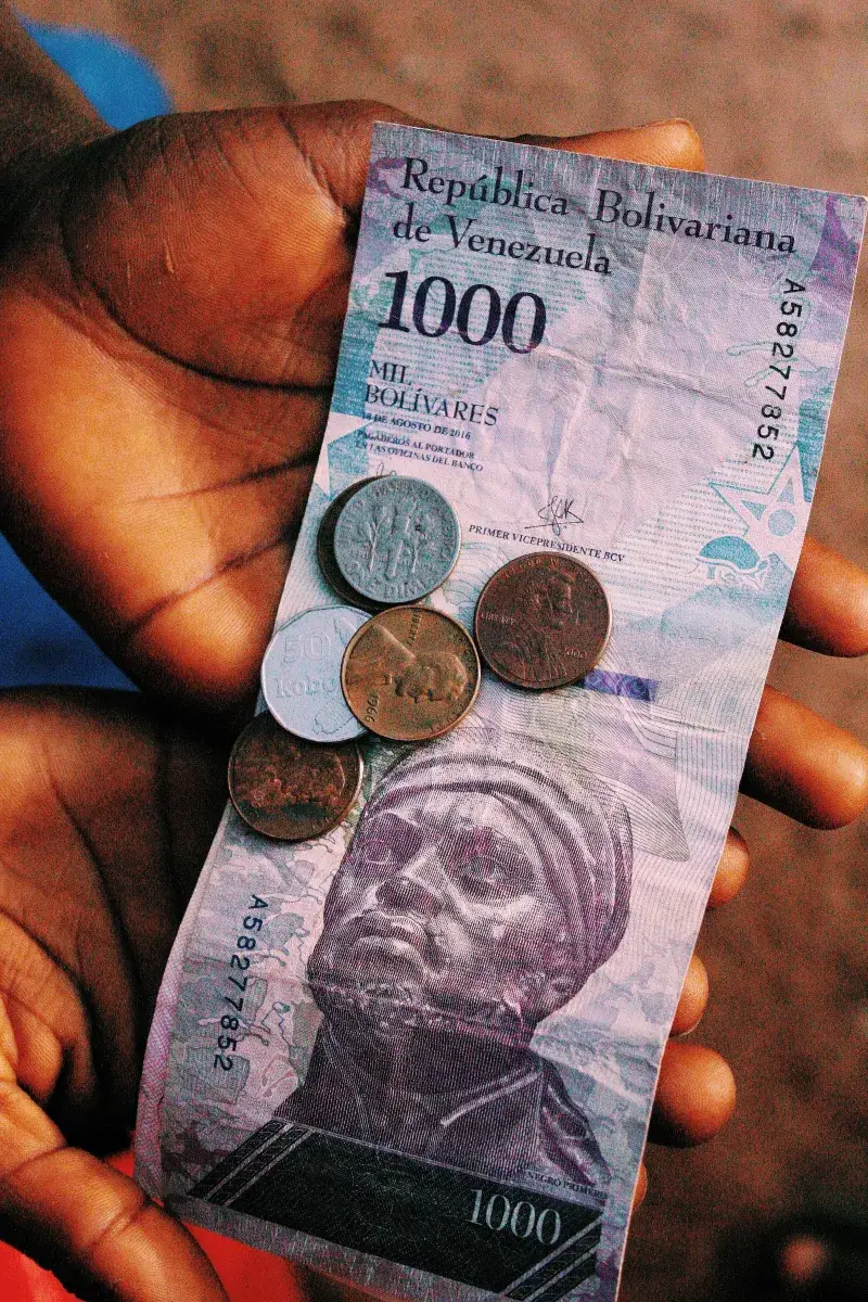 Close-up of hands holding a 1000 Bolivar banknote with coins, capturing the essence of Venezuelan currency.