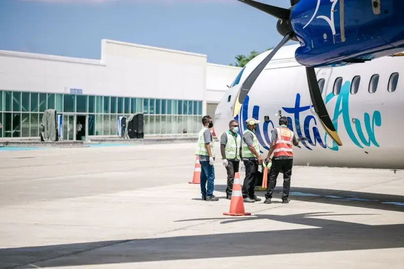 Ground crew in reflective vests preparing an airplane for departure at a sunny airport.