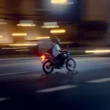 Un motociclista recorre una calle de la ciudad desenfocada por la noche, capturando el movimiento y las luces vibrantes.