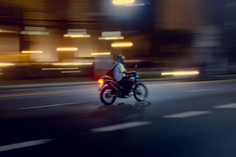 Un motociclista recorre una calle de la ciudad desenfocada por la noche, capturando el movimiento y las luces vibrantes.