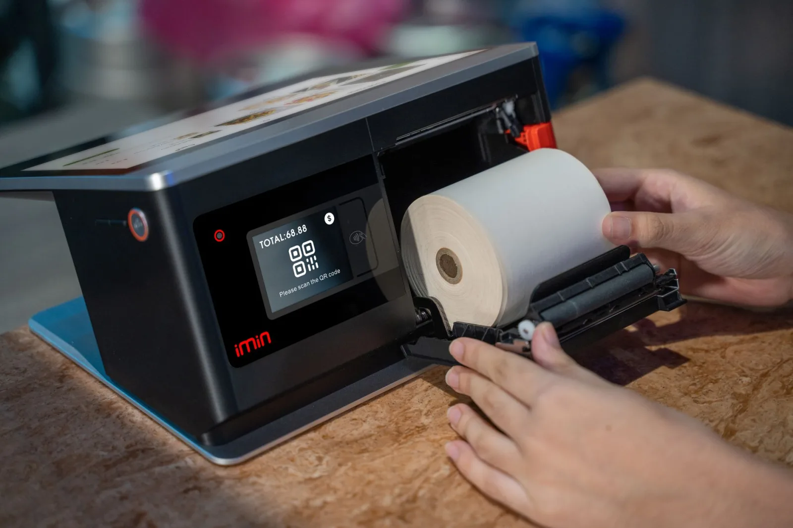 Manos colocando un rollo térmico en un dispositivo de punto de venta con pantalla táctil.