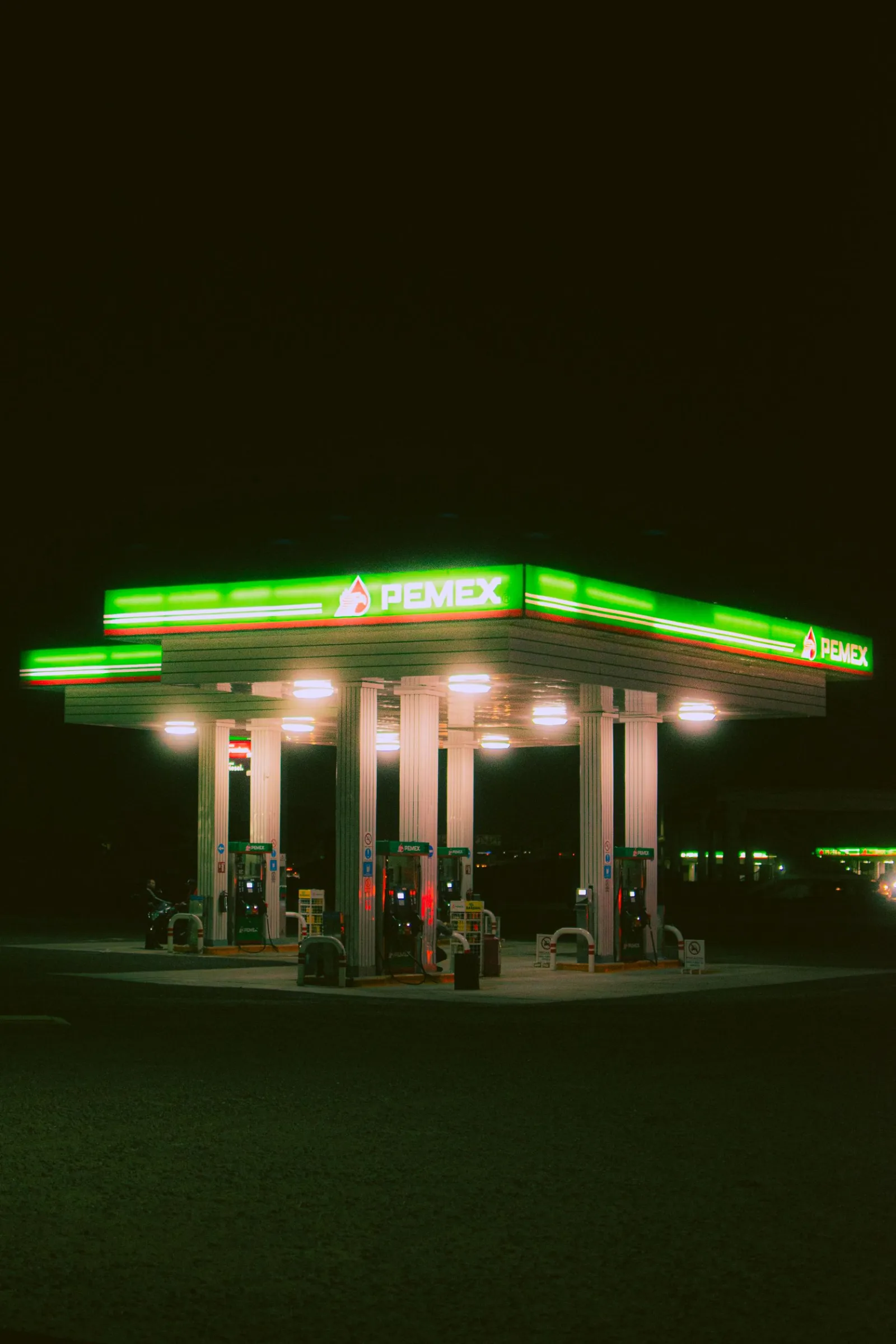Gasolinera Pemex iluminada con luces verdes brillantes contra el cielo nocturno, resaltando el tema de viaje