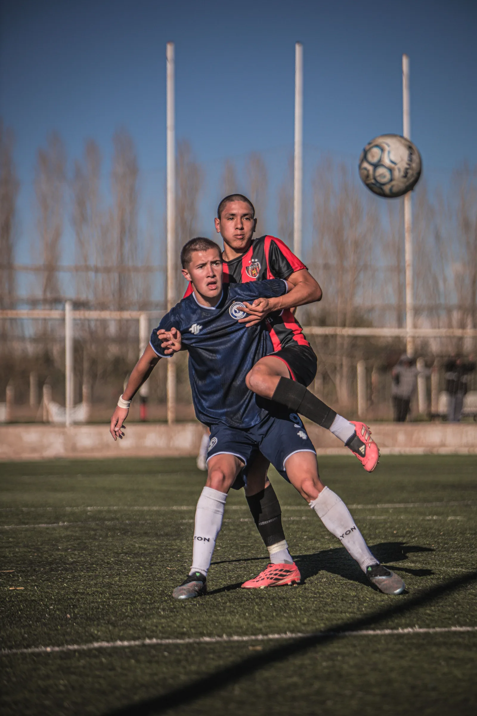 Dos jugadores de fútbol masculino compiten por el balón en un día soleado, mostrando su rendimiento atlético y la competencia.