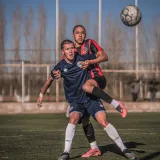 Dos jugadores de fútbol masculino compiten por el balón en un día soleado, mostrando su rendimiento atlético y la competencia.