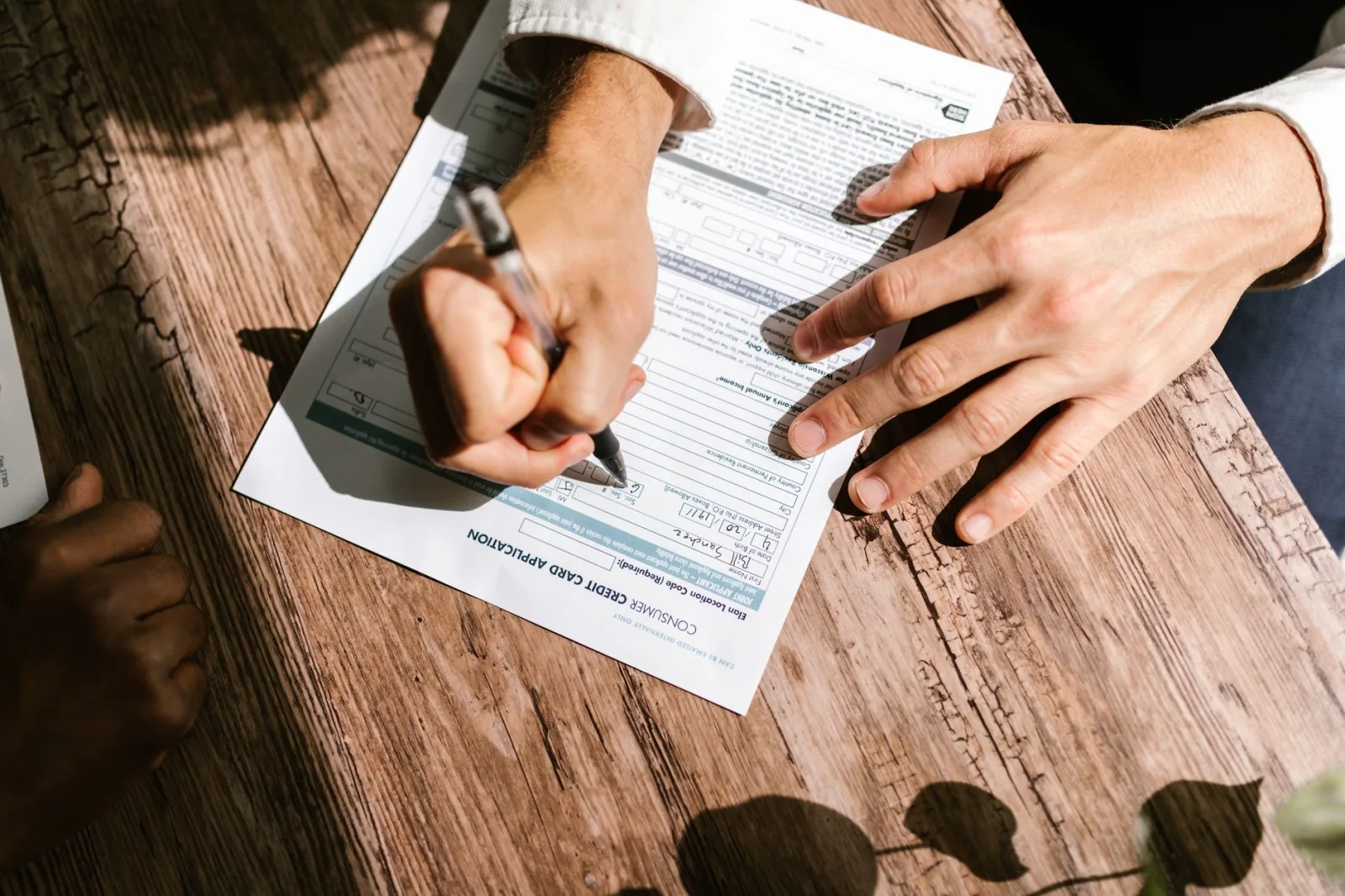 Manos escribiendo en un formulario de solicitud de crédito para un préstamo personal sobre una mesa de madera.