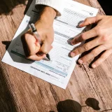 Manos escribiendo en un formulario de solicitud de crédito para un préstamo personal sobre una mesa de madera.