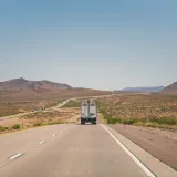 A highway scene with a truck driving through Arizona's desert landscape under a clear blue sky.