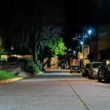 A serene nighttime street scene in Mérida, Venezuela, with parked cars and glowing streetlights.