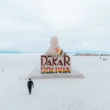 A solitary traveler approaches the Dakar Rally Monument in the vast Salar de Uyuni, Bolivia.