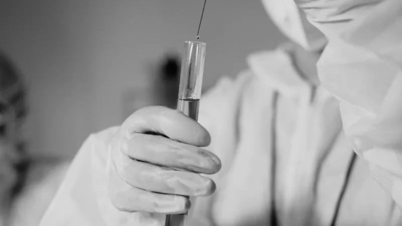 Científico con equipo de protección trabajando con un tubo de ensayo en un laboratorio.