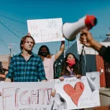 Protesters holding signs advocating equality and peace in an urban area.