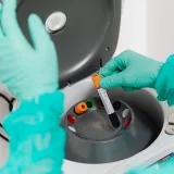 Un técnico de laboratorio con guantes utiliza una centrífuga para analizar sangre en un laboratorio moderno.