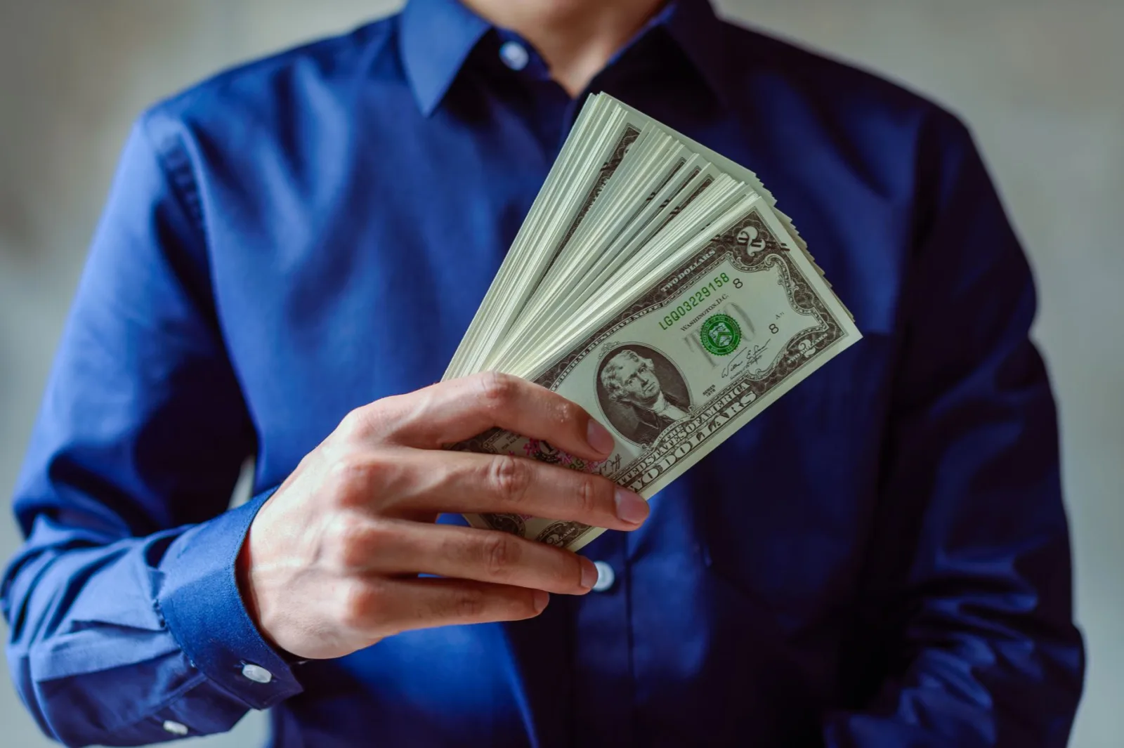 Primer plano de una persona con camisa azul sosteniendo varios billetes de dólares estadounidenses.