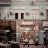 Busy city street with people passing by a Bitcoin exchange shop.