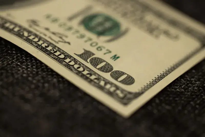Detailed close-up of a hundred dollar bill resting on dark fabric surface, showcasing texture.