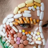 Primer plano de un rostro cubierto de píldoras y cápsulas coloridas, que representan medicación o salud.