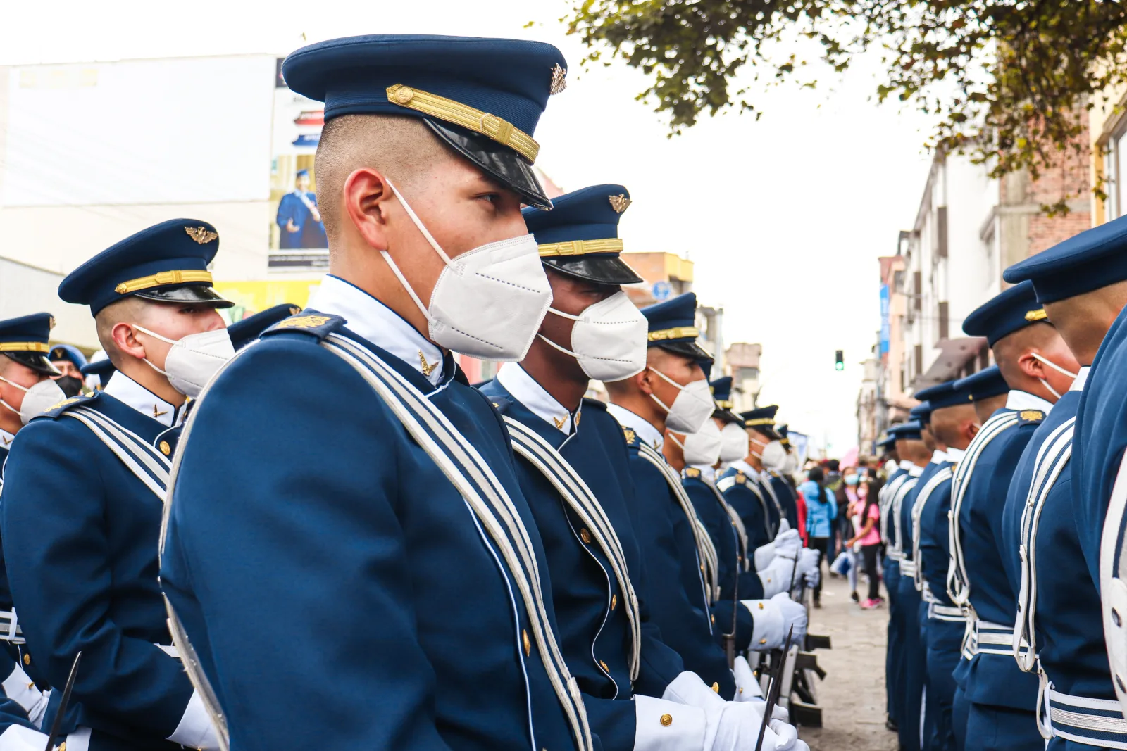 Soldados con uniformes ceremoniales y mascarillas desfilando por una calle de Ecuador.