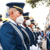 Soldados con uniformes ceremoniales y mascarillas desfilando por una calle de Ecuador.