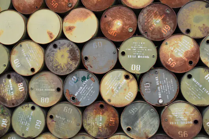Pile of old, rusty oil barrels stacked outdoors with visible labels and numbers.