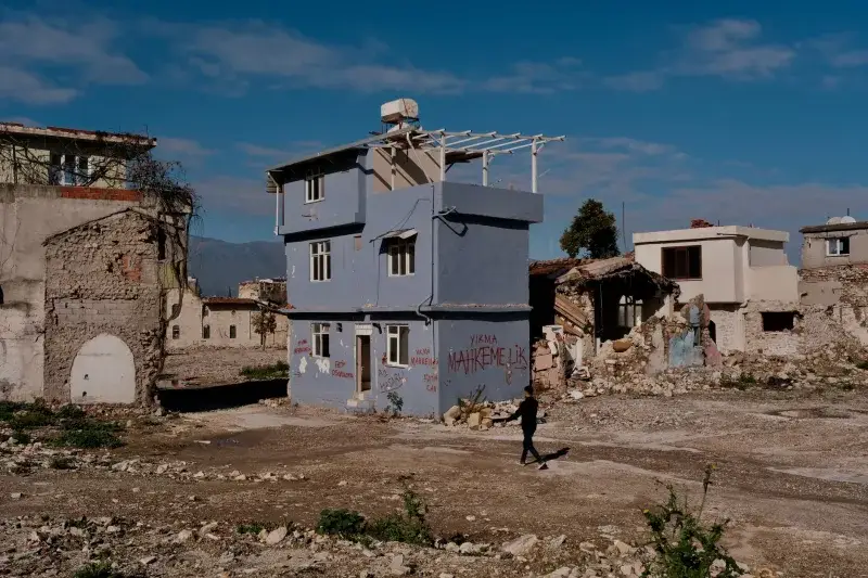 A man walks by a partially demolished house in a devastated urban landscape in Hatay, Türkiye.