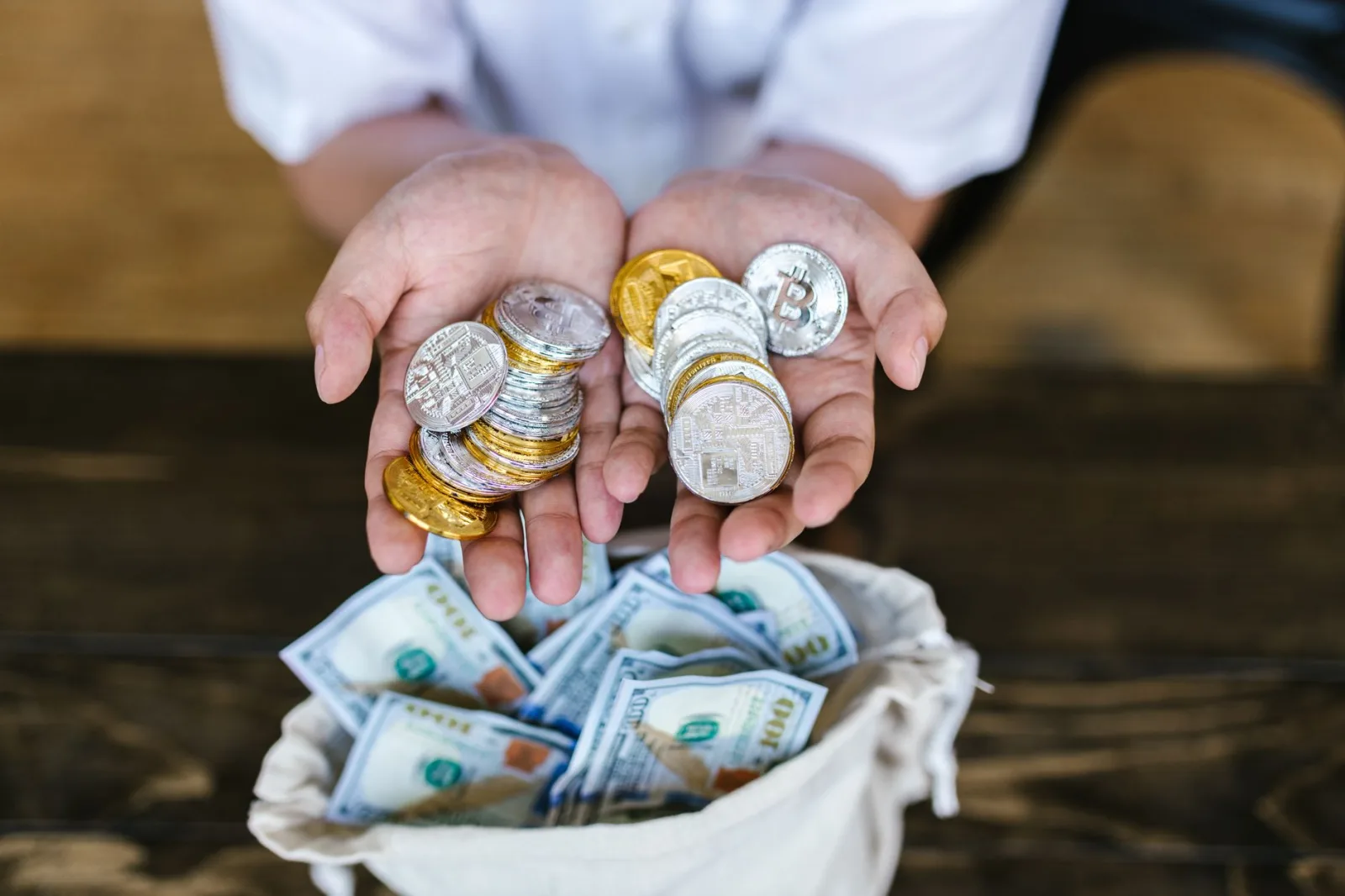 Persona sosteniendo monedas de criptomonedas sobre una bolsa de dinero en efectivo, simbolizando la convergencia de las finanzas digitales y tradicionales.