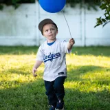 Niño pequeño disfrutando del verano al aire libre, sosteniendo un globo azul mientras lleva una camiseta de los Dodgers.