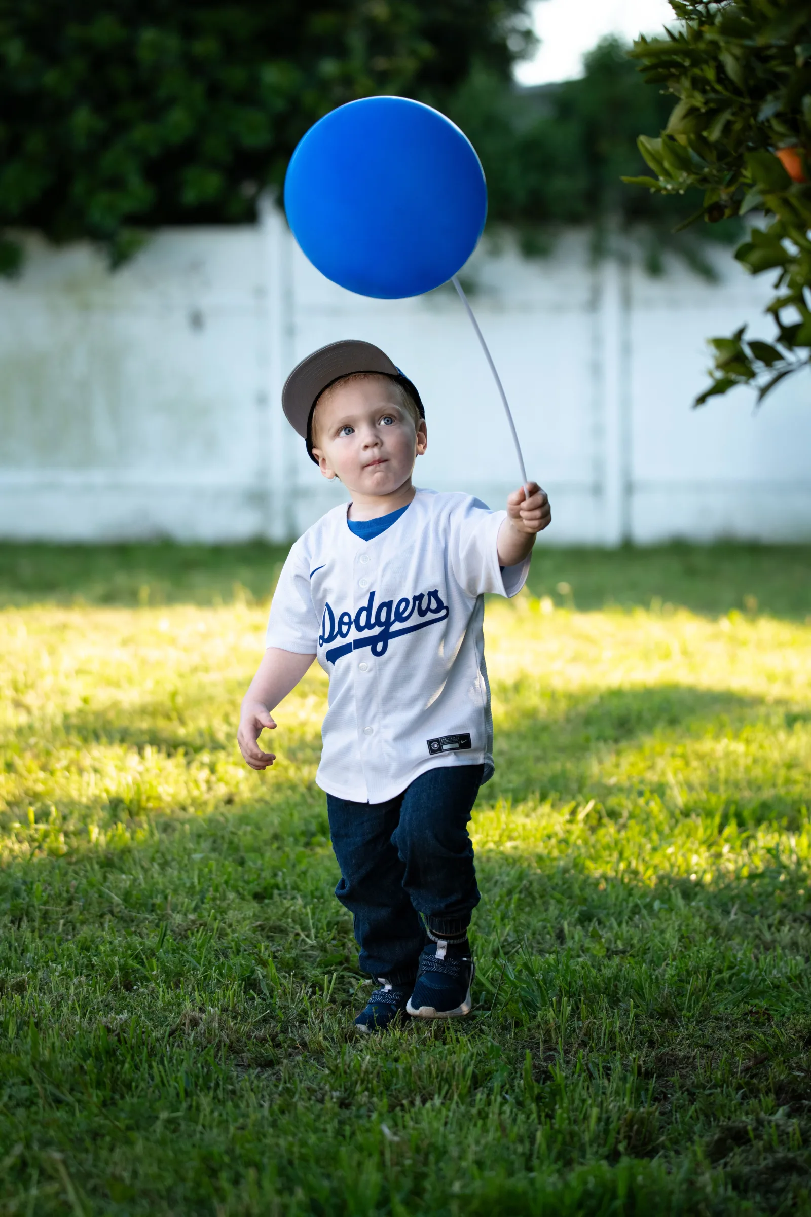Young child enjoying summer outdoors, holding a blue balloon while wearing a Dodgers jersey.