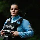 Female police officer in uniform standing outdoors with a confident expression and radio handset.
