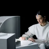 Una mujer en un entorno futurista trabajando en una computadora antigua, lo que sugiere una mezcla de pasado y futuro.