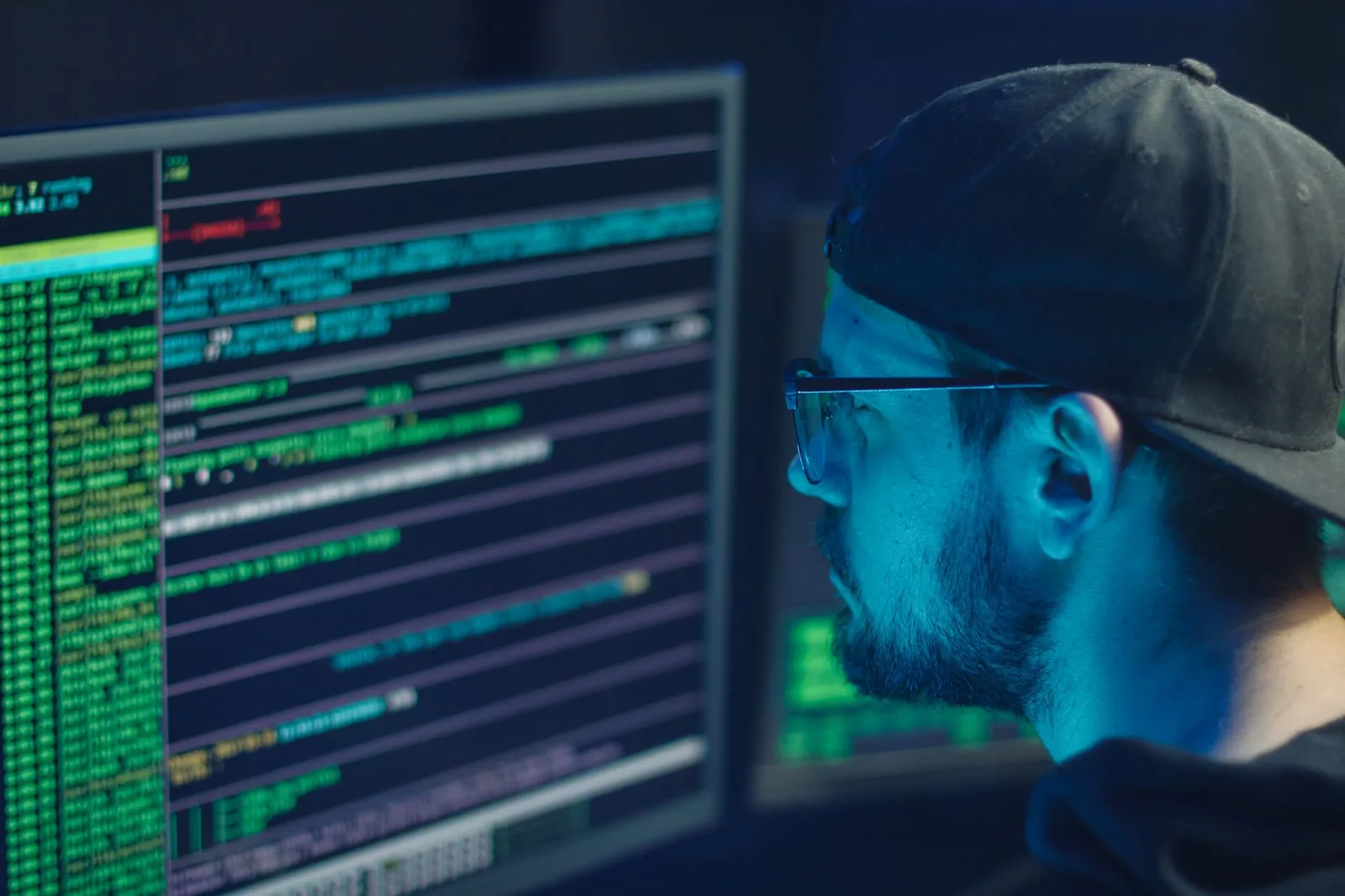 Un experto en ciberseguridad revisa líneas de código en varios monitores en una oficina con poca iluminación.