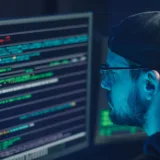 Un experto en ciberseguridad revisa líneas de código en varios monitores en una oficina con poca iluminación.