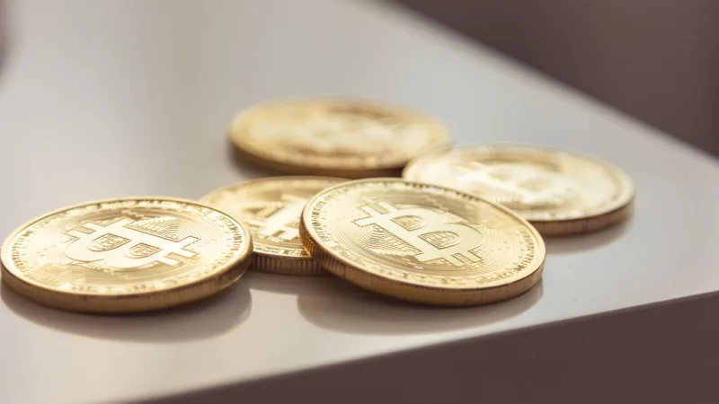 Primer plano de brillantes monedas de oro de Bitcoin sobre una superficie blanca, que simbolizan la riqueza en criptomonedas.