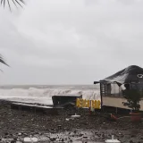 Un bar de playa costero dañado por una tormenta reciente, con olas altas, escombros y cielos nublados.