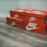 Red Nike shoe boxes stacked neatly on a wooden floor indoors.