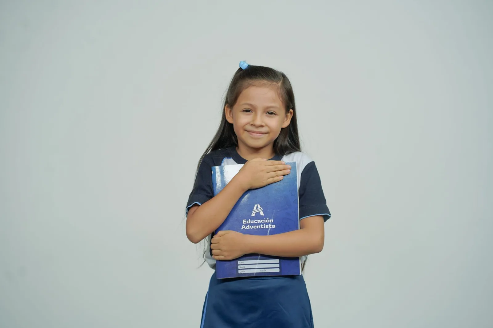 Una niña sonríe mientras sostiene su cuaderno escolar, como símbolo de la alegría de aprender.