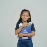 Una niña sonríe mientras sostiene su cuaderno escolar, como símbolo de la alegría de aprender.