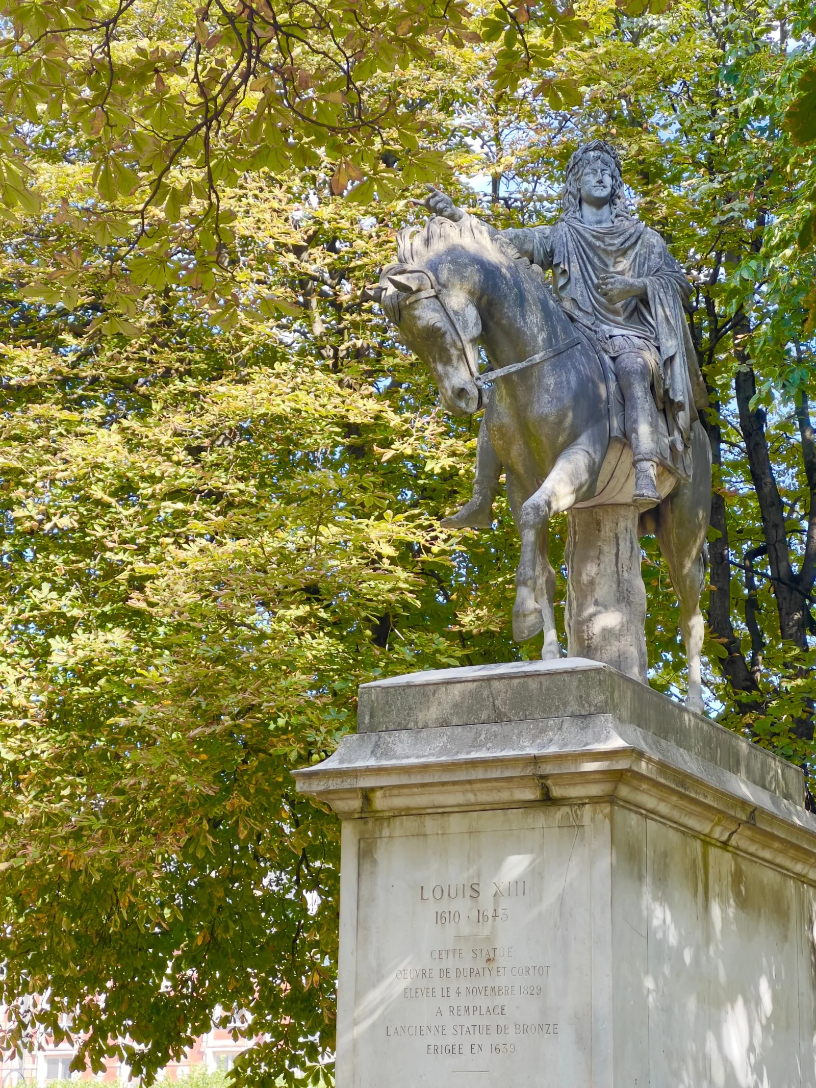 Estatua ecuestre de Luis XIV rodeada de frondosa vegetación de parque.